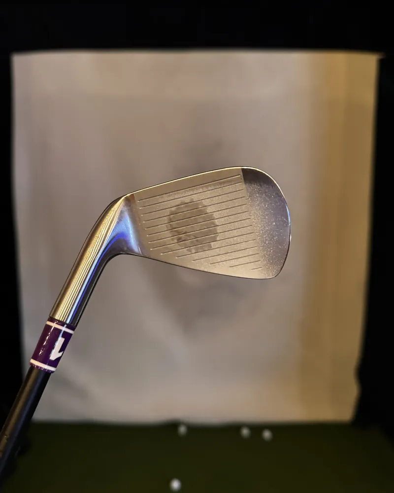 A seven-iron with a purple tape band on the shaft, held in front of an impact screen